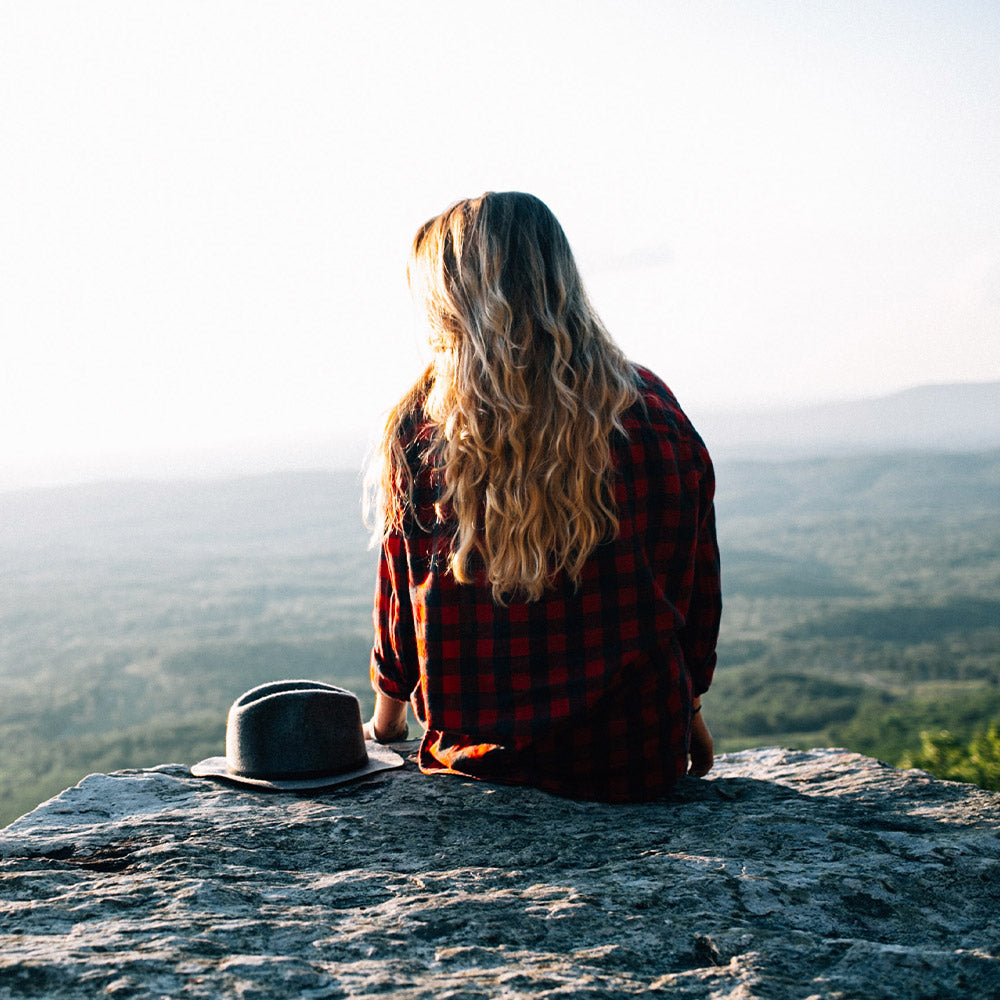 girl sitting on edge of hill with hat next to her