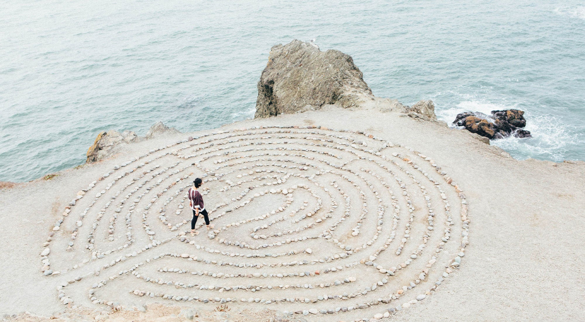 person walking besides beach and stone maze